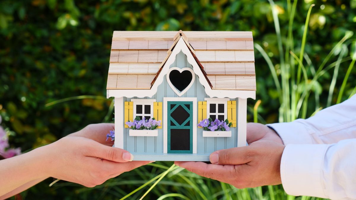 Mãos de um casal segurando uma miniatura de casa, símbolo da casa própria